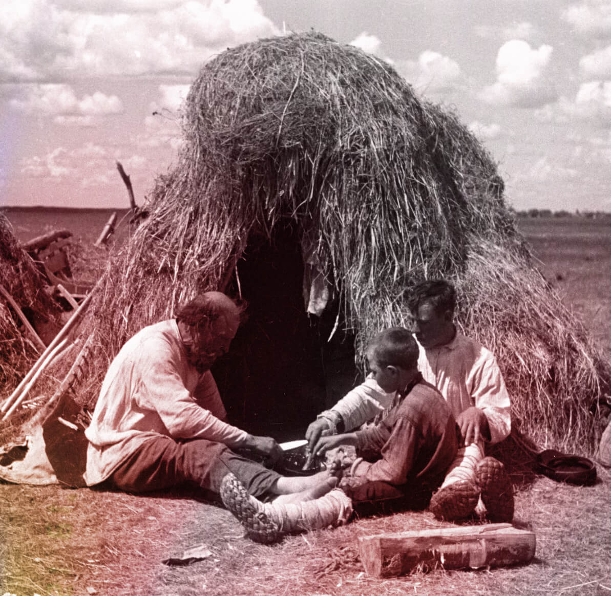 Фотография крестьян, сидящих перед соломенным шалашом